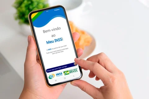Mão de uma pessoa segurando o celular e, na tela, o aplicativo Meu INSS